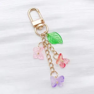 Detailed close-up of colorful gradient glass butterfly and leaf charms on a gold chain