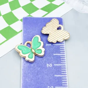 Detalle de los dijes de mariposa en esmalte verde sobre regla para referencia de talla
