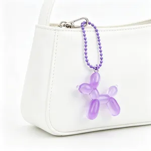 Close-up of a purple translucent balloon dog keychain hanging on a white handbag strap