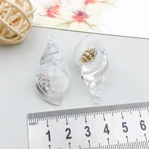 Close-up of transparent resin conch pendants next to a ruler for size reference