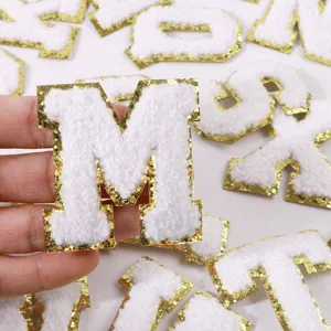 Close-up detail view of white chenille alphabet letter patch featuring shiny gold glitter border.