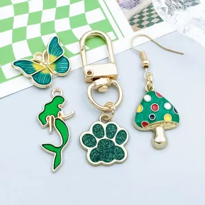 Foto macro detallada de dijes de esmalte verde: mariposa, sirena, pata de gato y hongo