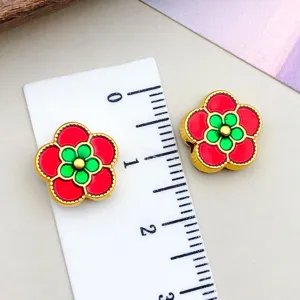 Detailed view of red and green enamel flower beads showing size scale with a ruler