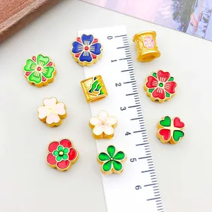 Detailed macro view of colorful enamel flower and clover charms next to a white ruler for scale