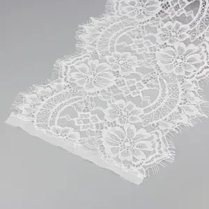 Detailed close-up of white floral lace fabric trim with delicate eyelash edges for wedding dress.