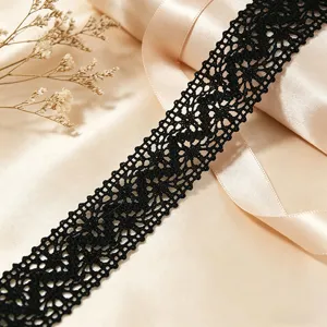 Detailed view of black cotton lace trim fabric, featuring delicate hollow-out floral crochet design.