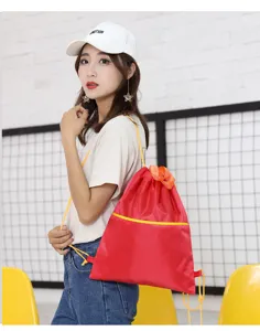 Detail view of red oxford cloth drawstring backpack with yellow straps for outdoor travel use.