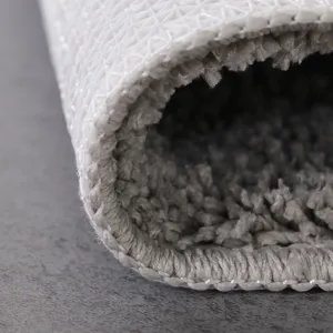 Close-up detail of grey tufted non-slip floor mat carpet with anti-slip backing edge.