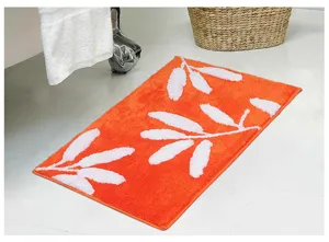 Détail de tapis de bain tufté orange avec texture absorbante douce et motif de feuilles blanches.