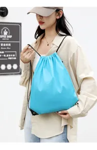 Blue drawstring backpack detail shot, lightweight polyester sports storage bag on model.