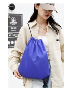 Detail view of blue polyester drawstring backpack worn by model in casual lifestyle scene.