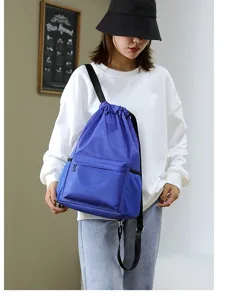 Detailed view of the blue nylon drawstring backpack showing the front zipper pocket and strap.