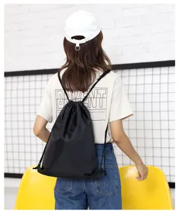 Detail shot of black drawstring backpack worn by model, showing polyester fabric and straps.