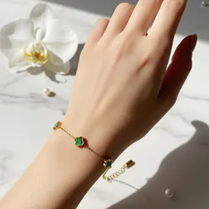 Detailaufnahme eines eleganten 18K Gold Kleeblatt Armbands am Handgelenk einer Frau.