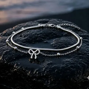 Detailed view of silver stainless steel double-layer anklet with bow pendant and beads