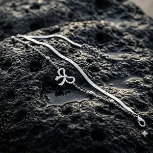 Detailed close-up of a stainless steel double-layered anklet with a bow pendant on dark rock