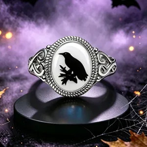 Primer plano de un anillo gótico plateado con una silueta de cuervo negro sobre blanco.