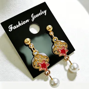 Detalle de pendientes de trébol dorado con flores de esmalte rojo y perlas