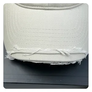 Close-up detail of distressed baseball cap brim with frayed edge and fine stitching.