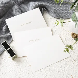 Biglietti augurali bianchi con testo dorato, design flatlay elegante per ogni festa.