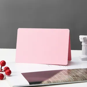 Close-up detail of a minimalist pink folded greeting card on a white desk with decor.