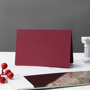 Close-up detail of a blank burgundy folded greeting card on a minimalist white desk with props.