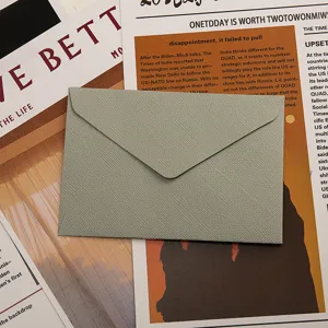 Vue détaillée d'une élégante enveloppe en papier texturé gris-vert sur un vieux journal.