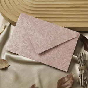 Detailed shot of retro pink tree texture paper envelope with natural leaves and wood tray.