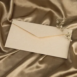 Detailansicht eines strukturierten beige Papierbriefumschlags auf goldenem Satin mit Trockenblumen.