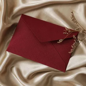 Detailed view of dark red textured envelope on glossy golden satin fabric with dry flower.