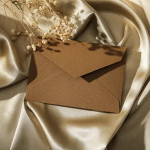 Vue détaillée d'une enveloppe marron vintage texturée en lin posée sur un tissu de soie dorée.