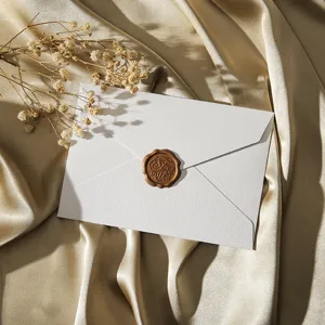 Enveloppe texturée blanche avec sceau de cire vintage et fleurs séchées sur fond satiné doré.