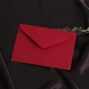 Gedetailleerd zicht op de rode linnen envelop met groen blad op donkere zijden achtergrond.