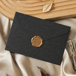 Detailed shot of a black vintage envelope with a gold wax seal on smooth satin fabric.
