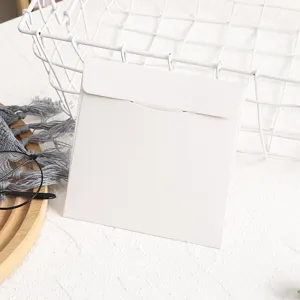Détail d'une pochette enveloppe carrée blanche pour CD en papier, design épuré et minimal.