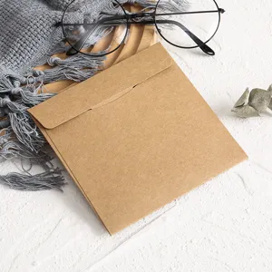 Vue rapprochée de la pochette CD en papier kraft carré posée sur un fond texturé blanc.
