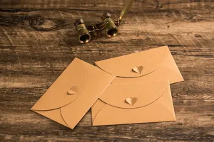 Close-up detail shot of vintage kraft paper envelopes featuring creative heart clasps on wood.