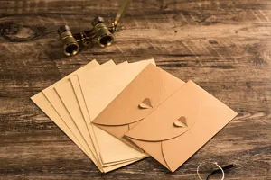 Detail view of vintage kraft paper envelopes and lined stationery sets with heart clasps on wood.