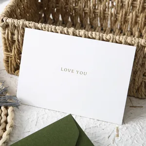 Dettaglio ravvicinato del biglietto di auguri bianco con testo d'amore e pratica busta verde.