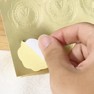 Détail d'autocollant cœur gaufré doré montrant le support pelable pour mariage.