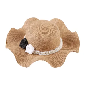 Women's straw sun hat with large wavy brim and pearl flower decorations.