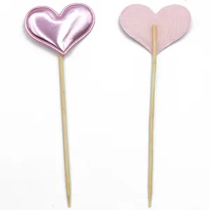 Detailed view of pink heart shaped dessert toppers with wooden sticks for party decorations.