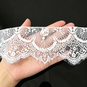 White eyelash lace trim detail close-up, delicate floral embroidery fabric for DIY sewing crafts.