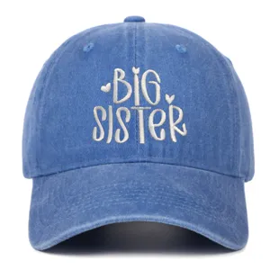 Detailopname van het witte BIG SISTER borduursel op een blauwe gewassen denim honkbalpet