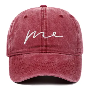 Detail view of a maroon washed cotton baseball cap with white 'me' cursive embroidery
