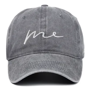 Close-up detail of a washed gray cotton baseball cap with white 'me' cursive embroidery