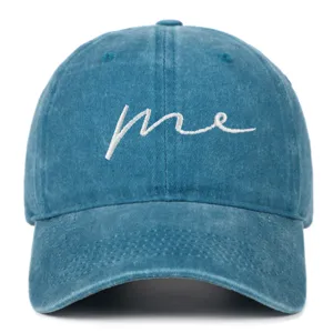 Close-up of washed blue denim baseball cap featuring white cursive 'me' embroidery detail.