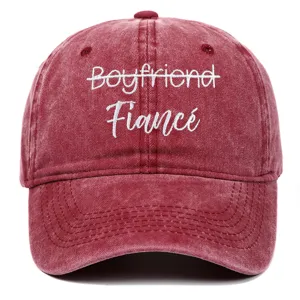 Macro view of white embroidery 'Fiancé' on a burgundy washed cotton baseball cap.