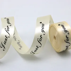 Vue détaillée d'un ruban en satin beige de 25 mm, imprimé d'un texte noir pour emballage cadeau.