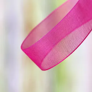 Close up macro view of bright pink organza ribbon, sheer fabric detail for gift wrapping.